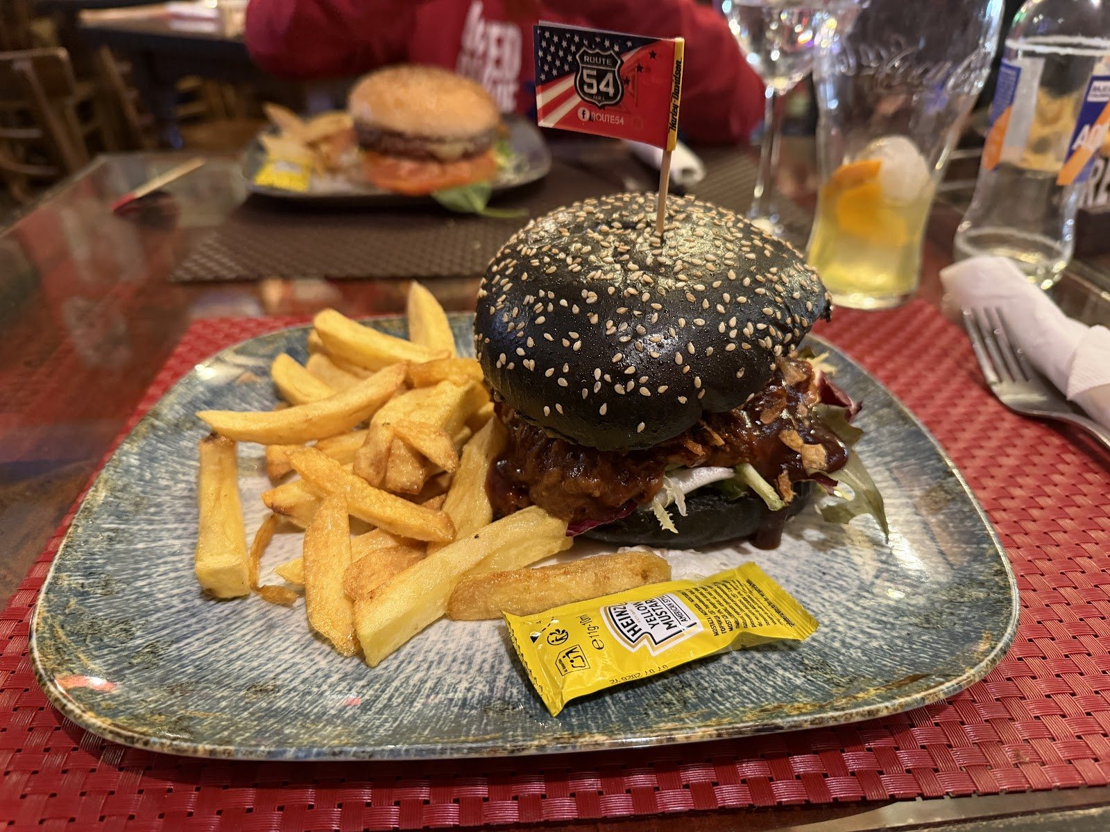 Hamburguesa especial con pan negro de sésamo, acompañada de patatas fritas y mostaza.